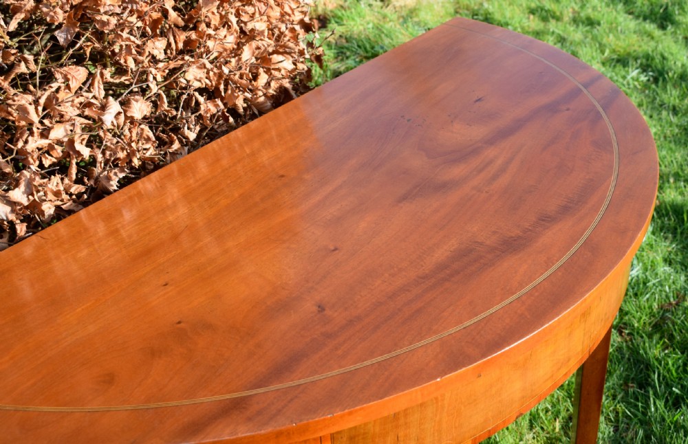 A Georgian mahogany demi-lune console table featuring a semi-circular top with string inlay and three tapered legs. View XI