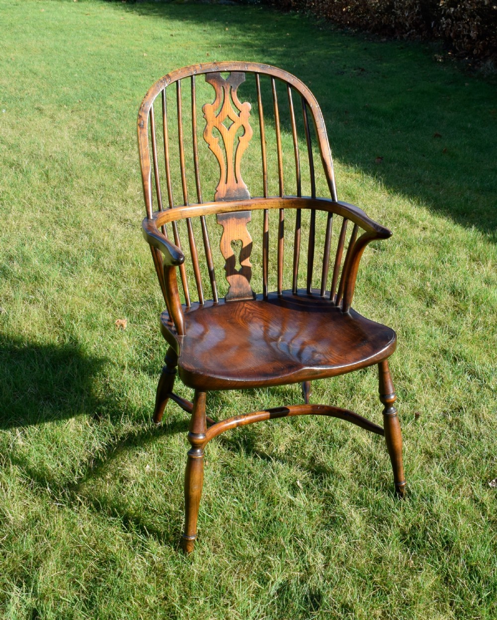 An antique dark wood Windsor armchair featuring a hoop back, pierced central splat, turned legs, and a shaped seat. View V