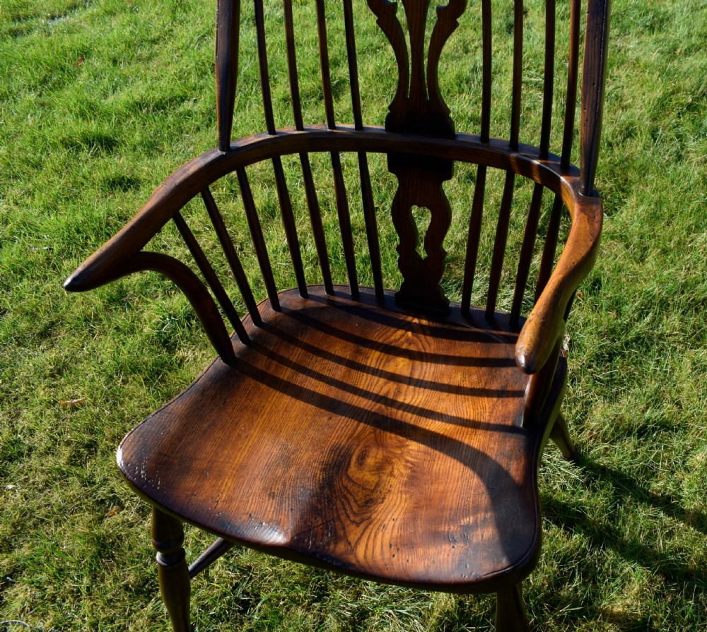 An antique dark wood Windsor armchair featuring a hoop back, pierced central splat, turned legs, and a shaped seat. View X