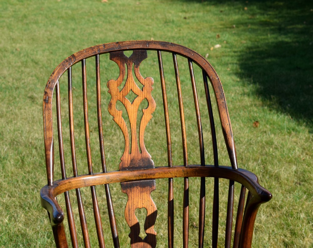 An antique dark wood Windsor armchair featuring a hoop back, pierced central splat, turned legs, and a shaped seat. View XIV