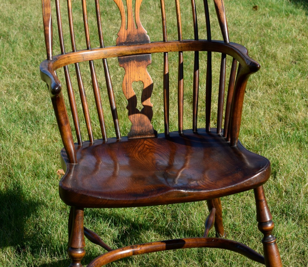 An antique dark wood Windsor armchair featuring a hoop back, pierced central splat, turned legs, and a shaped seat. View XV