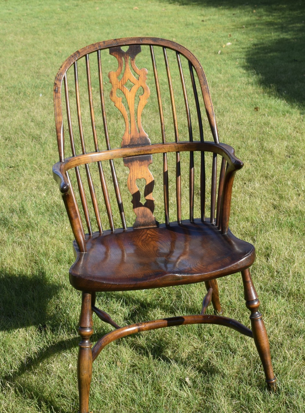 An antique dark wood Windsor armchair featuring a hoop back, pierced central splat, turned legs, and a shaped seat. View XVI
