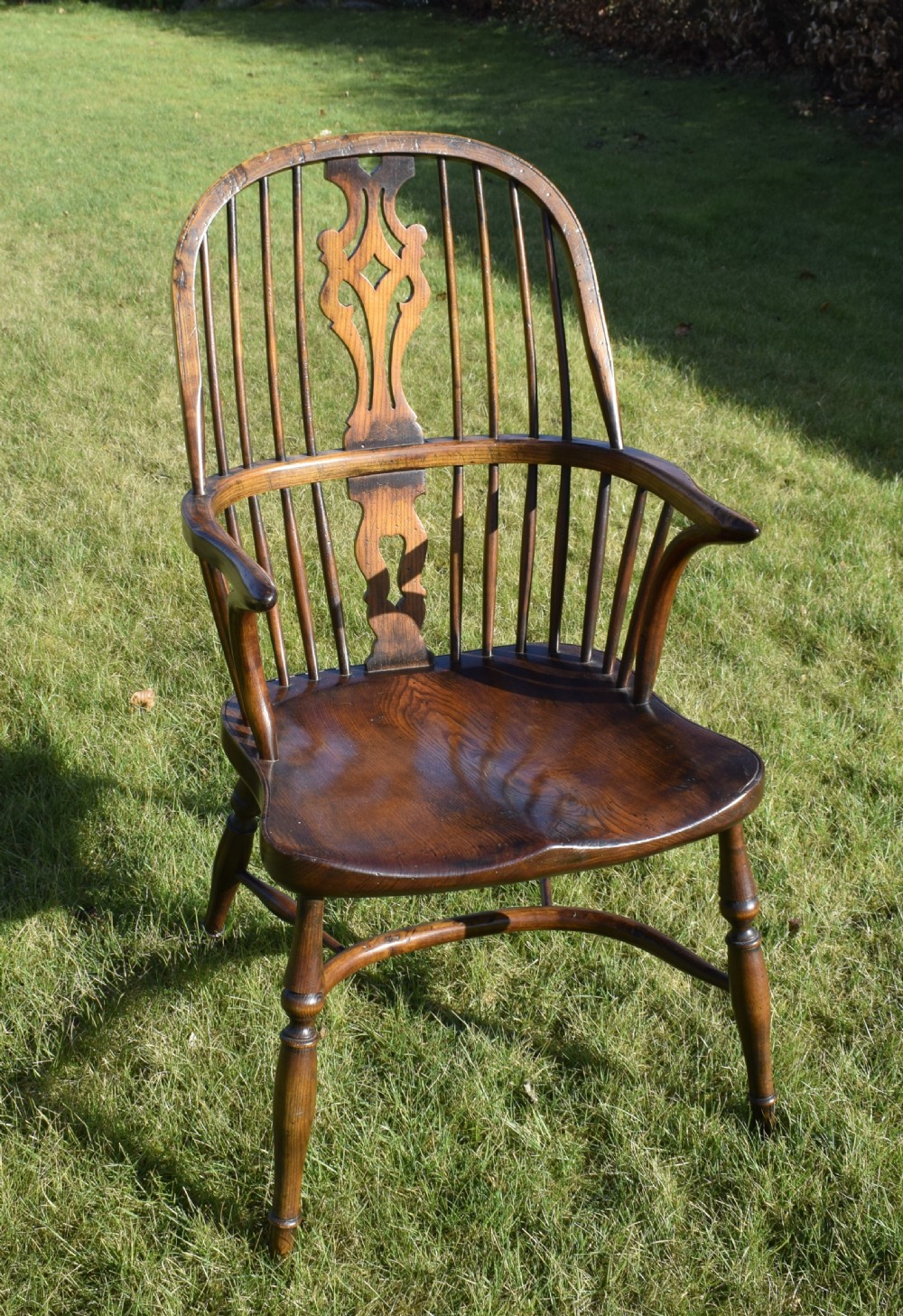 An antique dark wood Windsor armchair featuring a hoop back, pierced central splat, turned legs, and a shaped seat. View XVIII