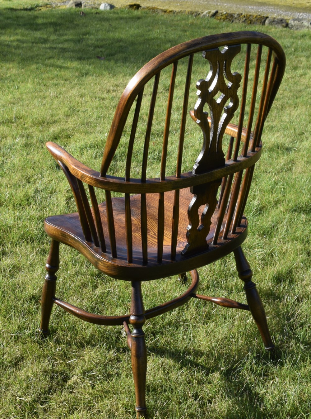 An antique dark wood Windsor armchair featuring a hoop back, pierced central splat, turned legs, and a shaped seat. View XIX