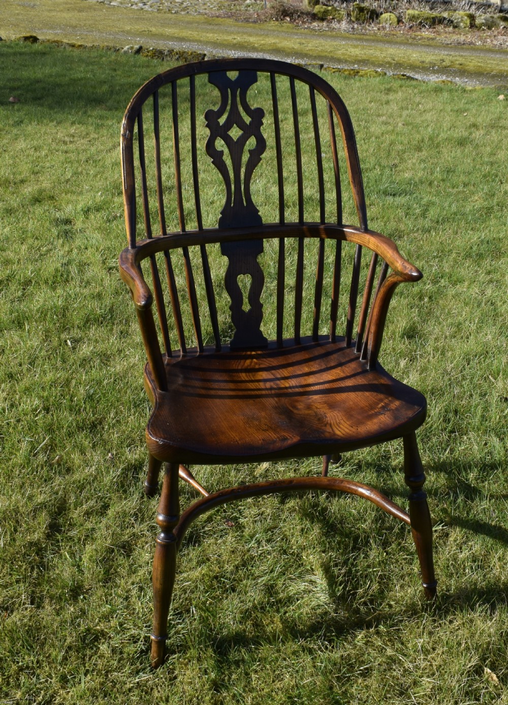 An antique dark wood Windsor armchair featuring a hoop back, pierced central splat, turned legs, and a shaped seat. View XX