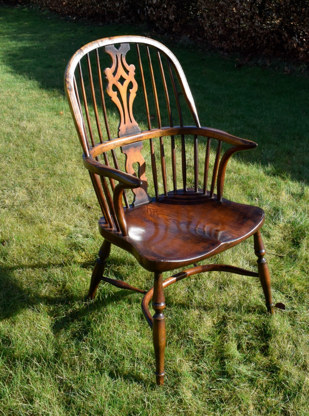 An antique dark wood Windsor armchair featuring a hoop back, pierced central splat, turned legs, and a shaped seat. View XXI