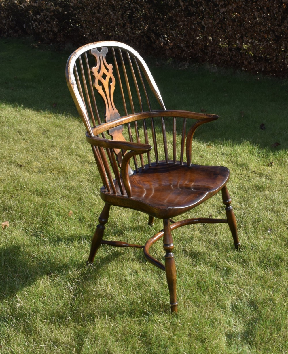 An antique dark wood Windsor armchair featuring a hoop back, pierced central splat, turned legs, and a shaped seat.