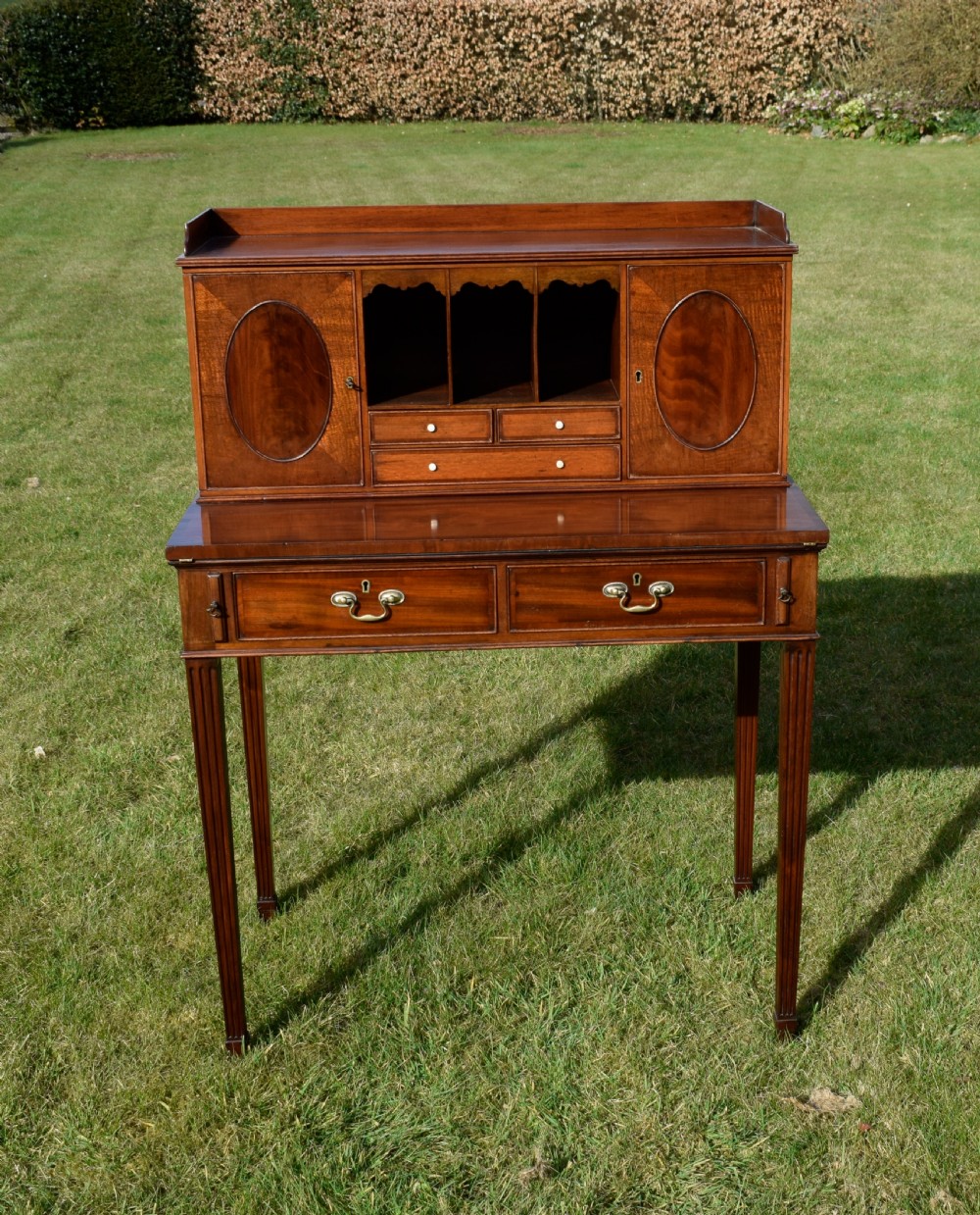 An Edwardian mahogany writing desk featuring a top superstructure with pigeonholes, cupboards, and small drawers above two frieze drawers on fluted tapered legs.