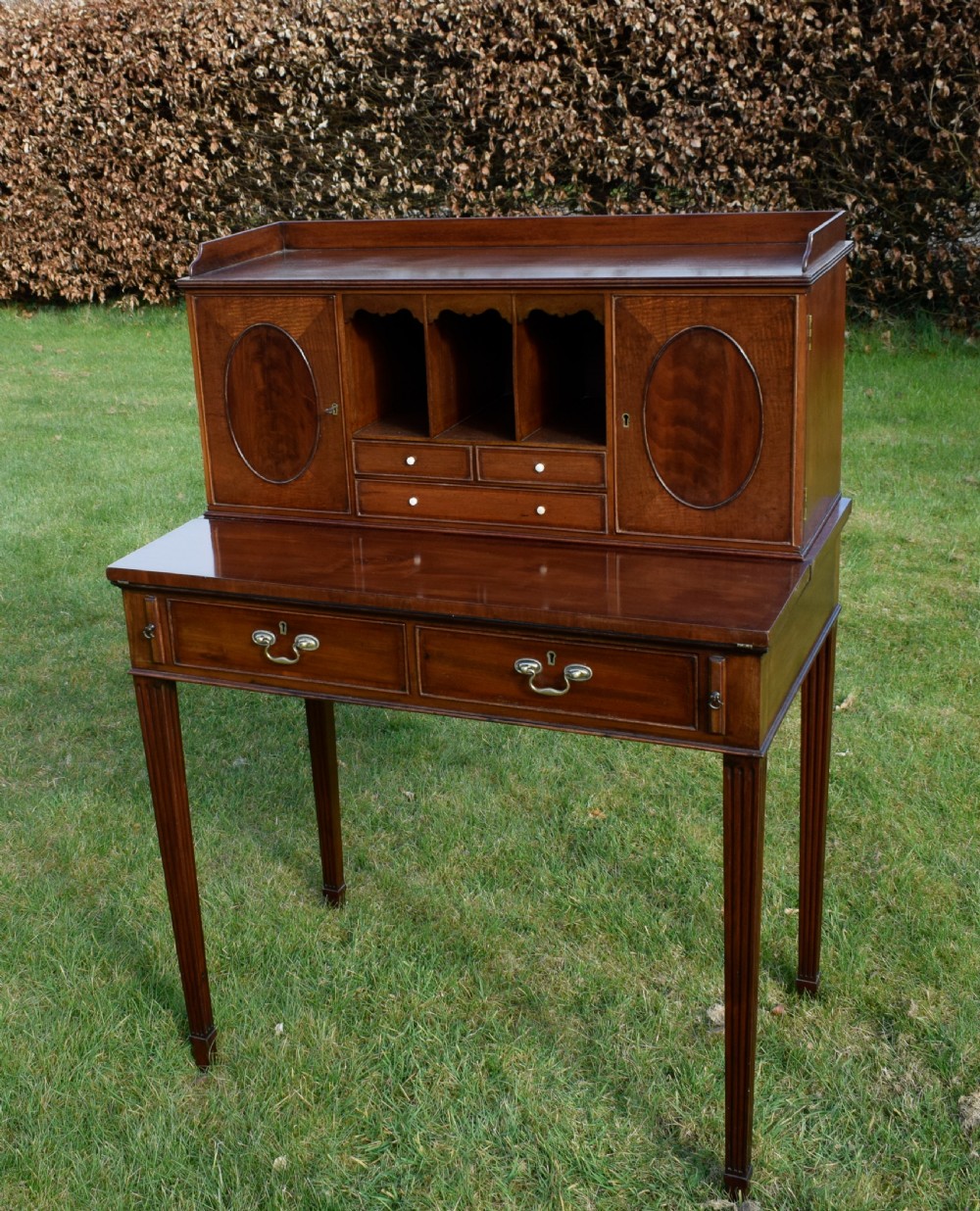 An Edwardian mahogany writing desk featuring a top superstructure with pigeonholes, cupboards, and small drawers above two frieze drawers on fluted tapered legs. View II