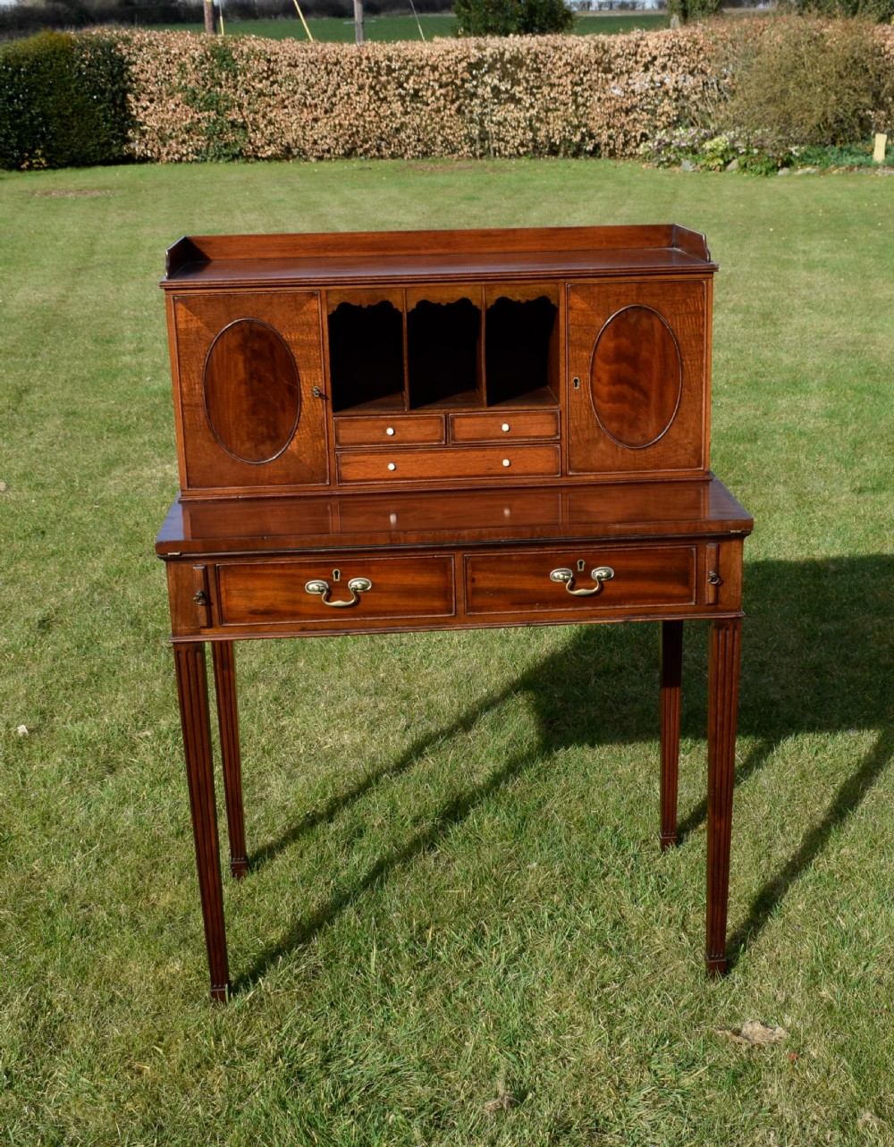 An Edwardian mahogany writing desk featuring a top superstructure with pigeonholes, cupboards, and small drawers above two frieze drawers on fluted tapered legs. View III