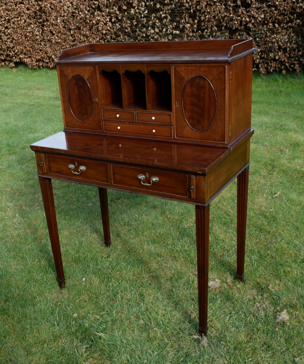 An Edwardian mahogany writing desk featuring a top superstructure with pigeonholes, cupboards, and small drawers above two frieze drawers on fluted tapered legs. View V