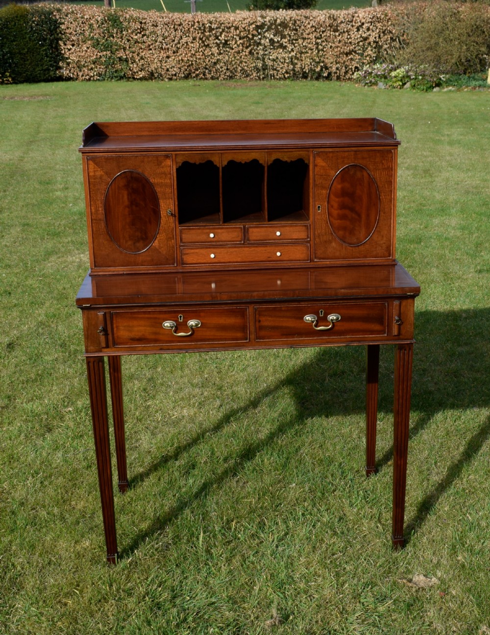 An Edwardian mahogany writing desk featuring a top superstructure with pigeonholes, cupboards, and small drawers above two frieze drawers on fluted tapered legs. View VI