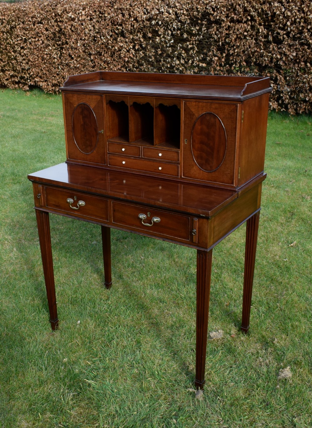 An Edwardian mahogany writing desk featuring a top superstructure with pigeonholes, cupboards, and small drawers above two frieze drawers on fluted tapered legs. View VII