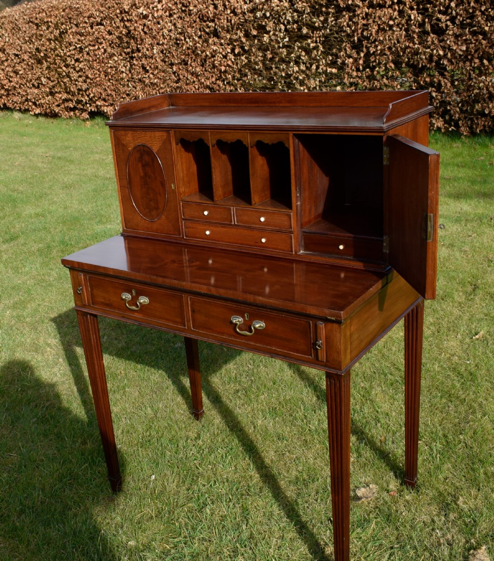 An Edwardian mahogany writing desk featuring a top superstructure with pigeonholes, cupboards, and small drawers above two frieze drawers on fluted tapered legs. View IX