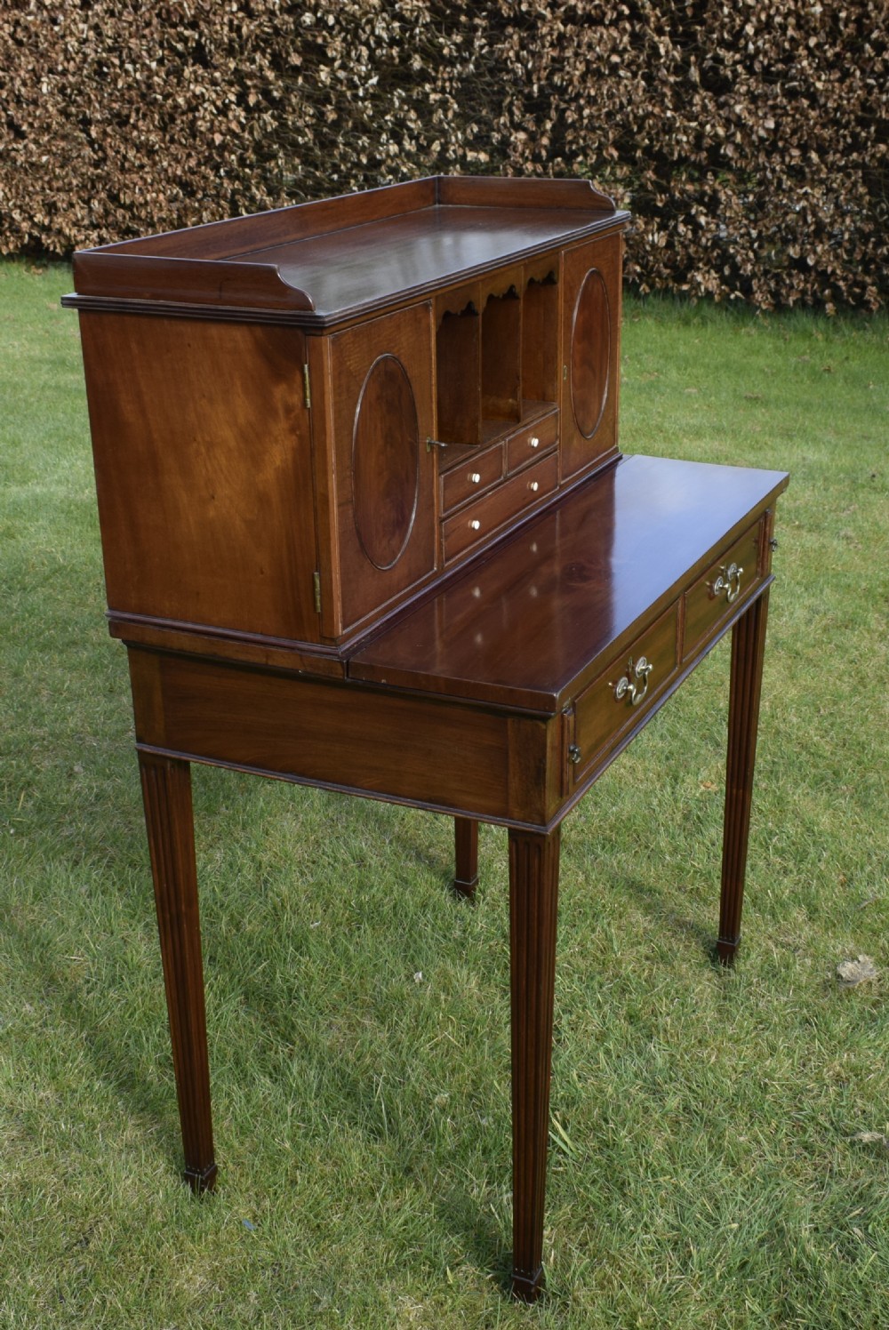An Edwardian mahogany writing desk featuring a top superstructure with pigeonholes, cupboards, and small drawers above two frieze drawers on fluted tapered legs. View X