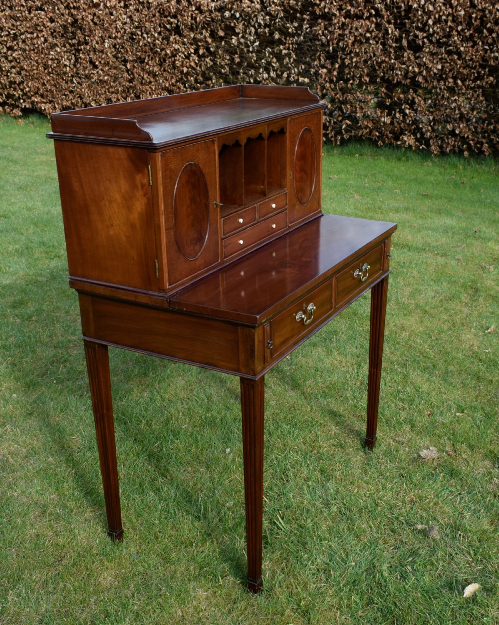 An Edwardian mahogany writing desk featuring a top superstructure with pigeonholes, cupboards, and small drawers above two frieze drawers on fluted tapered legs. View XI