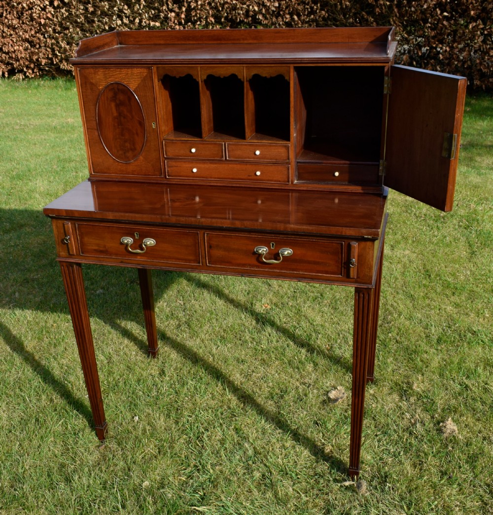 An Edwardian mahogany writing desk featuring a top superstructure with pigeonholes, cupboards, and small drawers above two frieze drawers on fluted tapered legs. View XVI