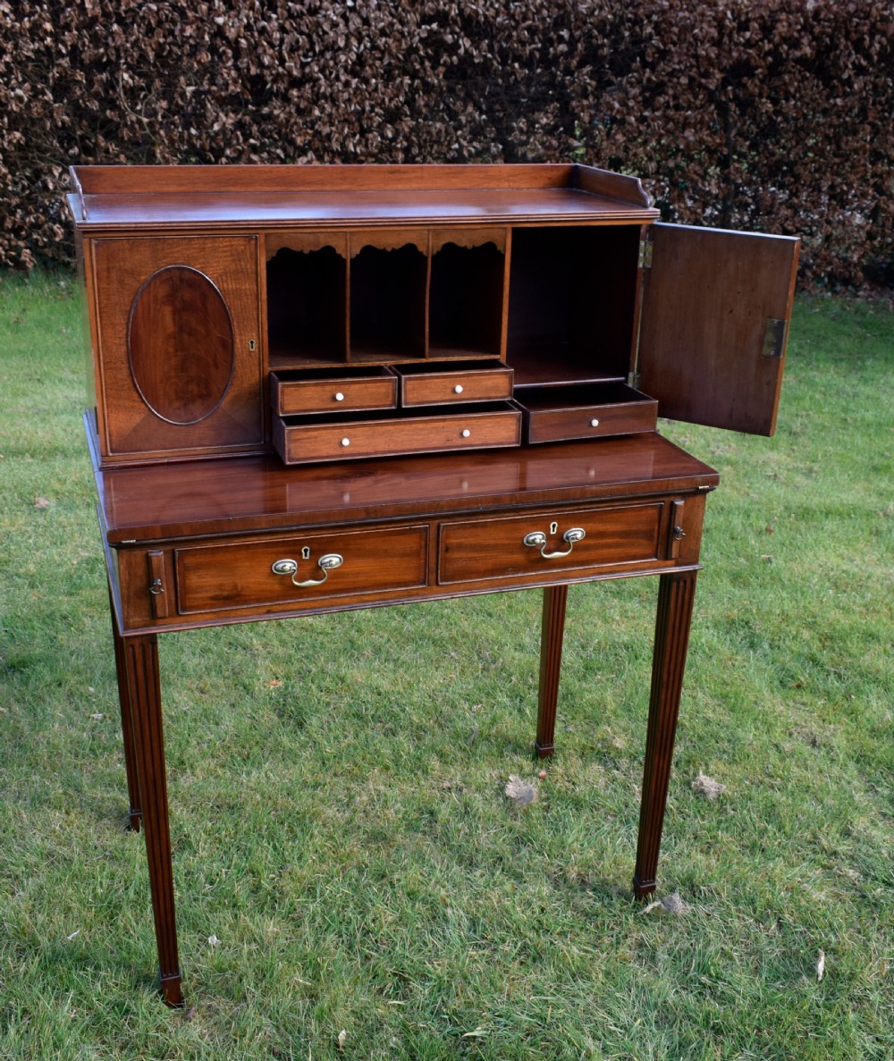 An Edwardian mahogany writing desk featuring a top superstructure with pigeonholes, cupboards, and small drawers above two frieze drawers on fluted tapered legs. View XVII