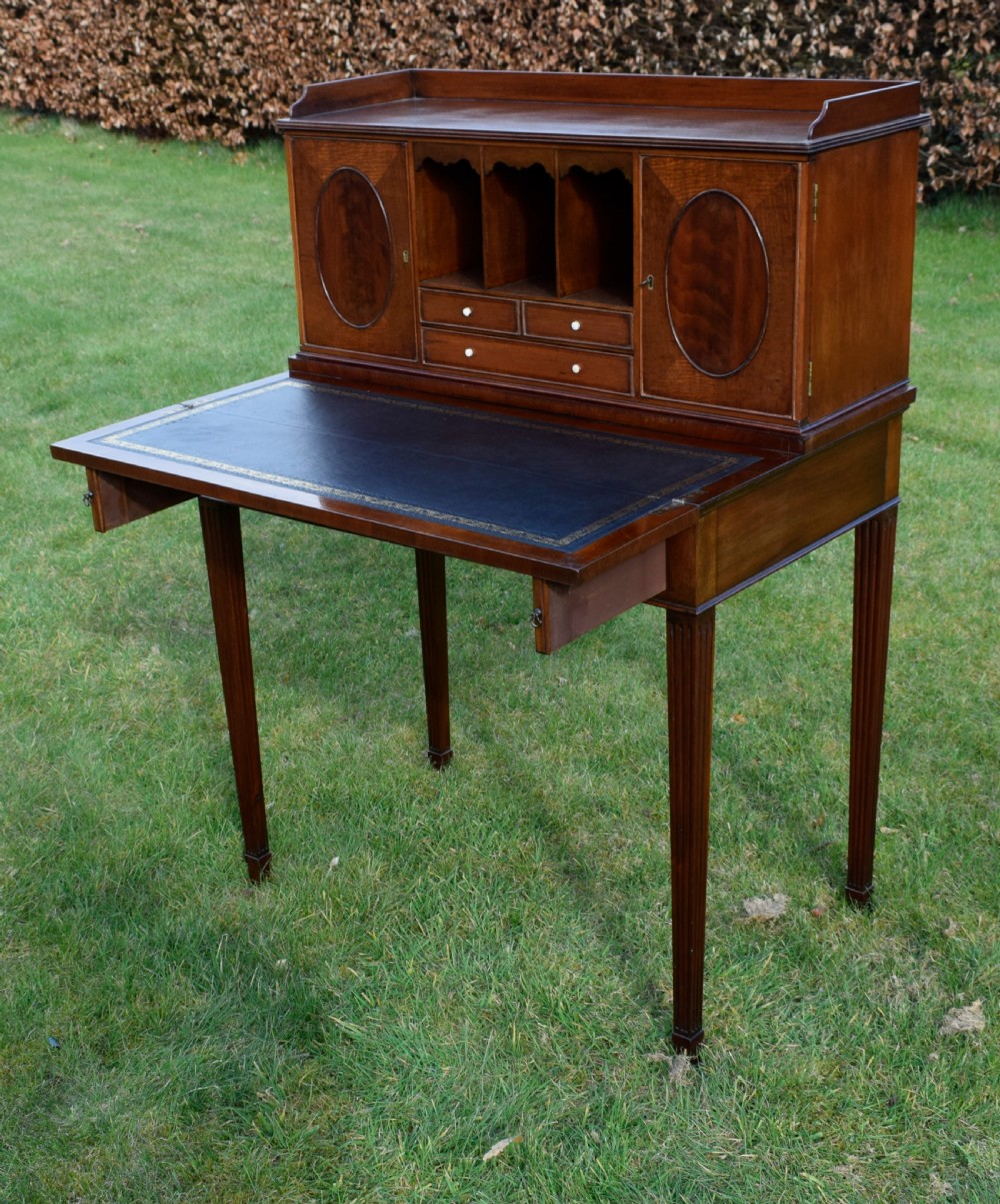 An Edwardian mahogany writing desk featuring a top superstructure with pigeonholes, cupboards, and small drawers above two frieze drawers on fluted tapered legs. View XIX