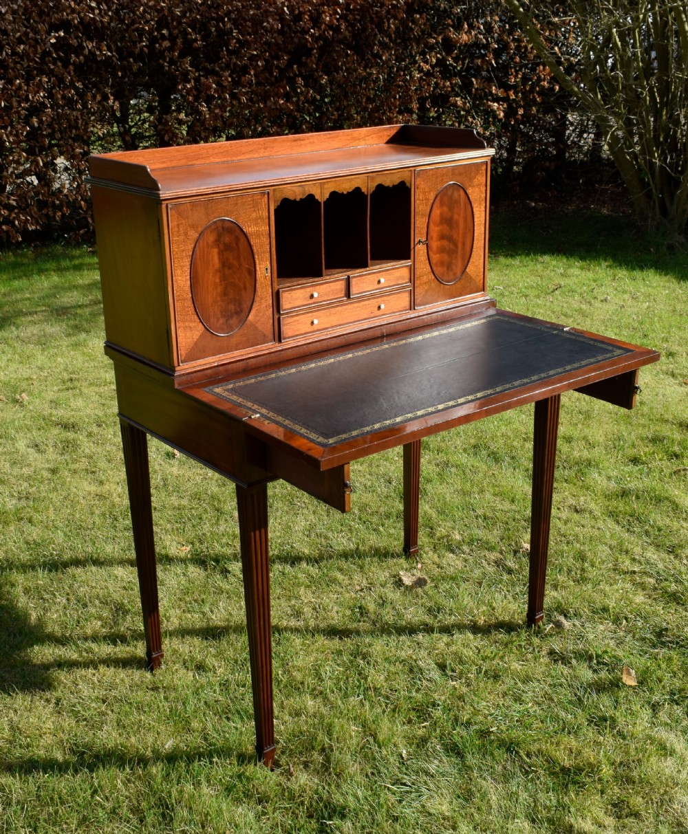 An Edwardian mahogany writing desk featuring a top superstructure with pigeonholes, cupboards, and small drawers above two frieze drawers on fluted tapered legs. View XXVI