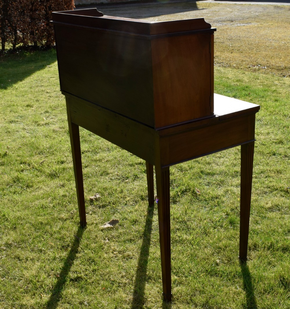 An Edwardian mahogany writing desk featuring a top superstructure with pigeonholes, cupboards, and small drawers above two frieze drawers on fluted tapered legs. View XXIX