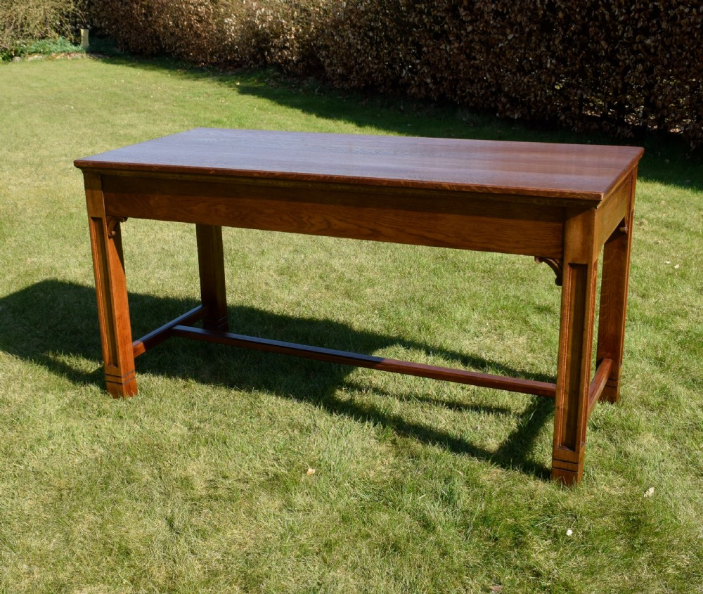An early 20th-century warm brown rectangular oak dining table featuring square legs with carved detailing and a central low stretcher frame.