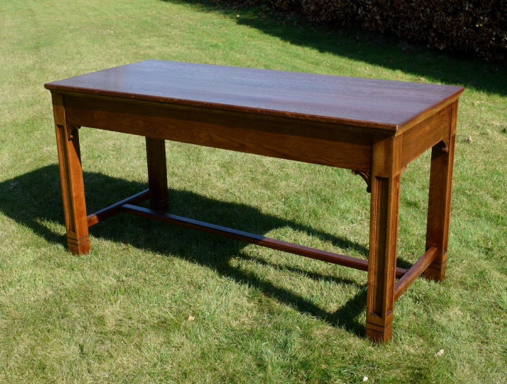 An early 20th-century warm brown rectangular oak dining table featuring square legs with carved detailing and a central low stretcher frame. View VII