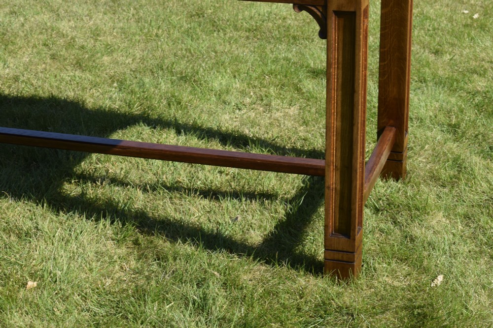 An early 20th-century warm brown rectangular oak dining table featuring square legs with carved detailing and a central low stretcher frame. View X