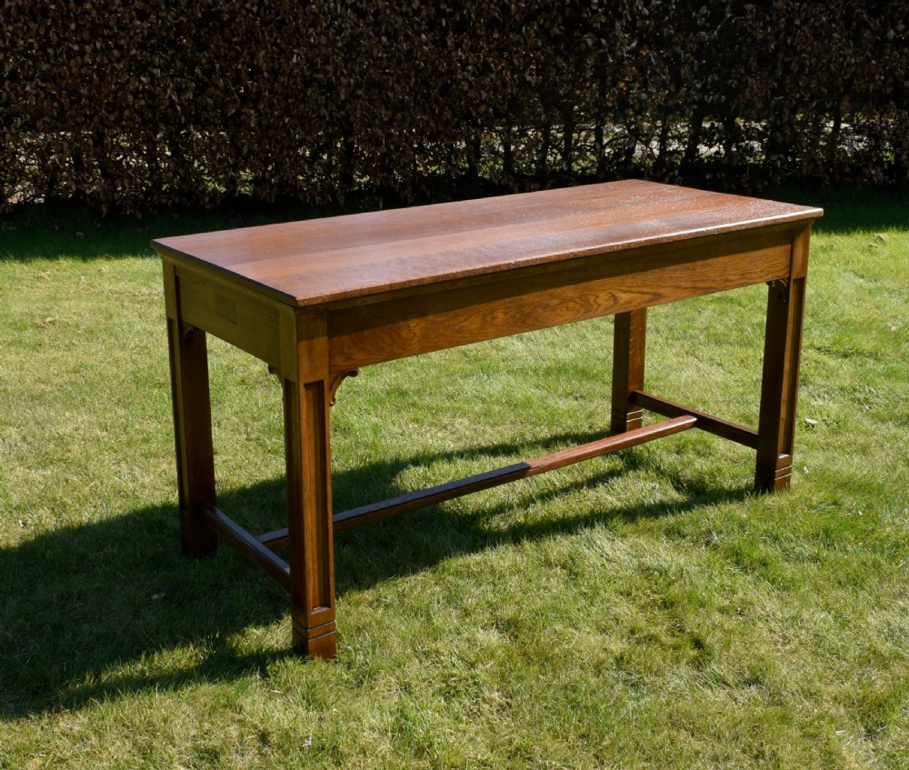 An early 20th-century warm brown rectangular oak dining table featuring square legs with carved detailing and a central low stretcher frame. View XI