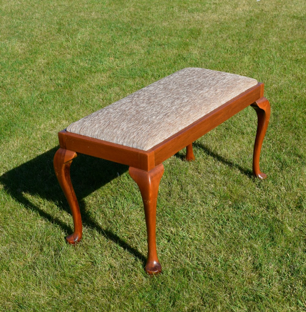An early 20th-century duet stool with a woven fabric seat and warm brown mahogany cabriole legs.