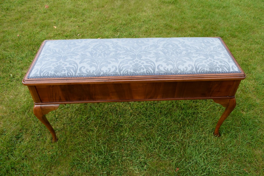 An elongated rectangular wooden duet piano stool featuring cabriole legs and a blue patterned damask upholstered seat trimmed with dark braid.