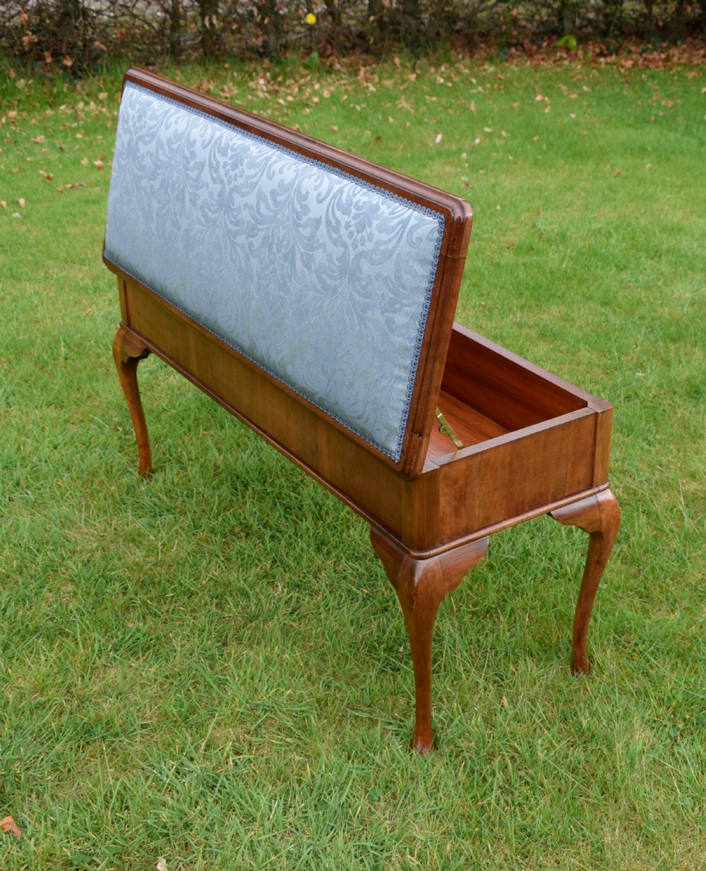 An elongated rectangular wooden duet piano stool featuring cabriole legs and a blue patterned damask upholstered seat trimmed with dark braid. View XX