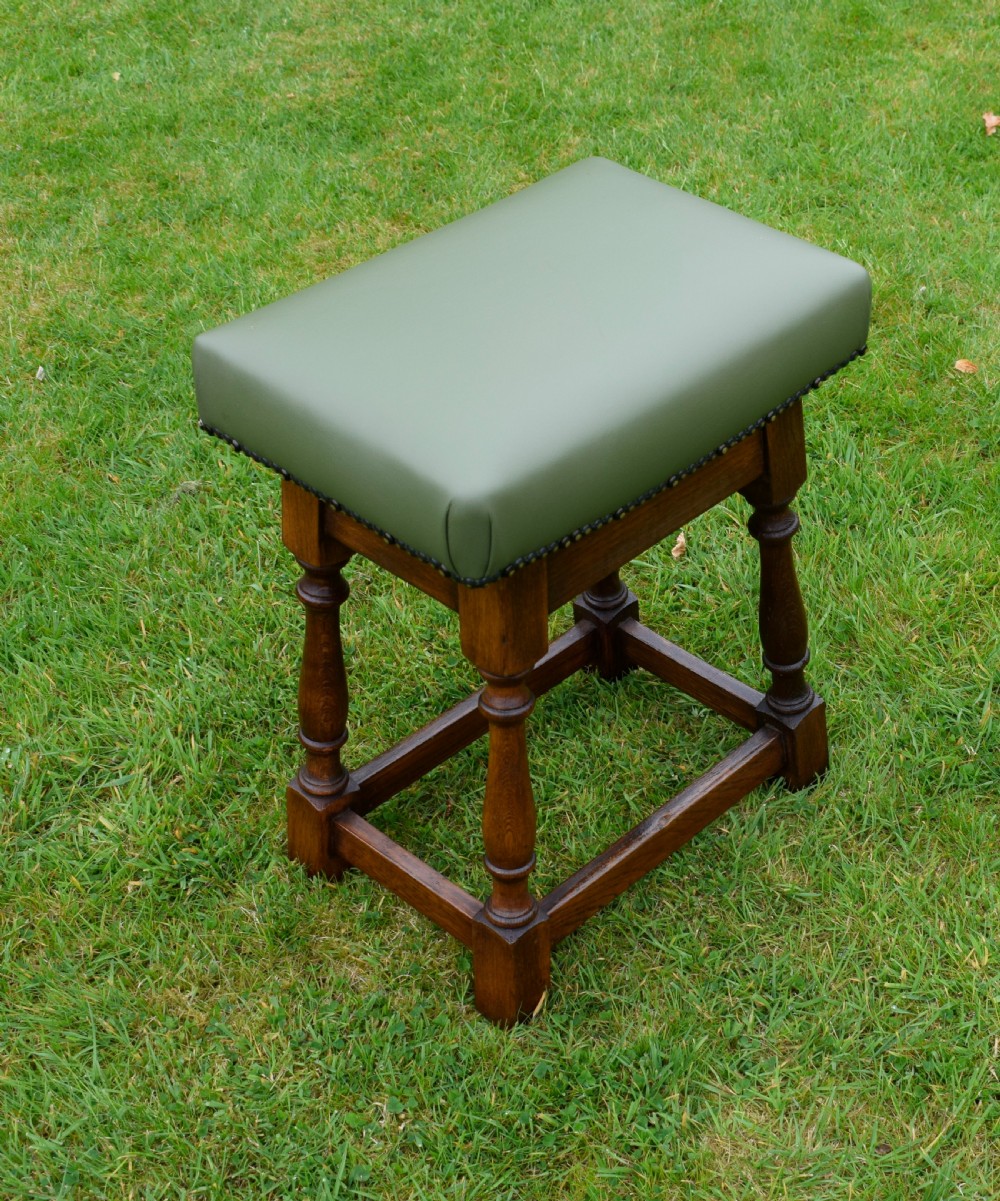 An early twentieth-century oak joint stool featuring an olive green leather upholstered seat secured with brass studs over turned legs.