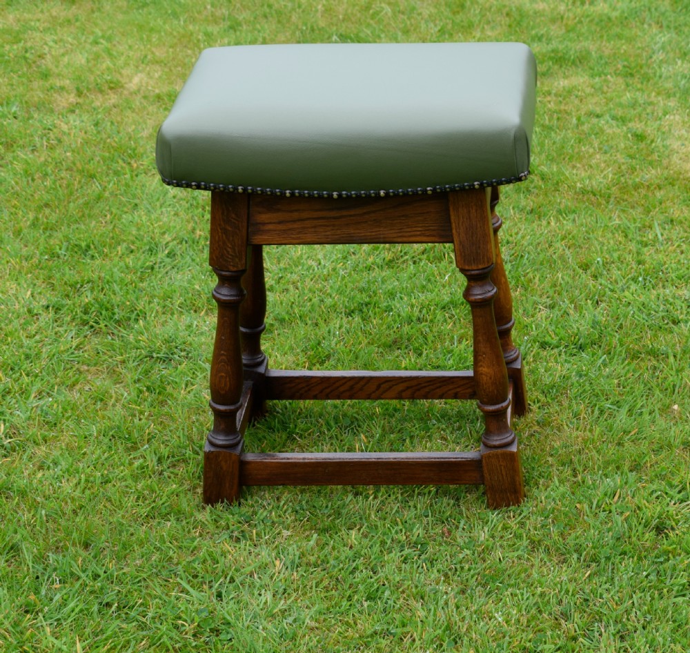An early twentieth-century oak joint stool featuring an olive green leather upholstered seat secured with brass studs over turned legs. View III