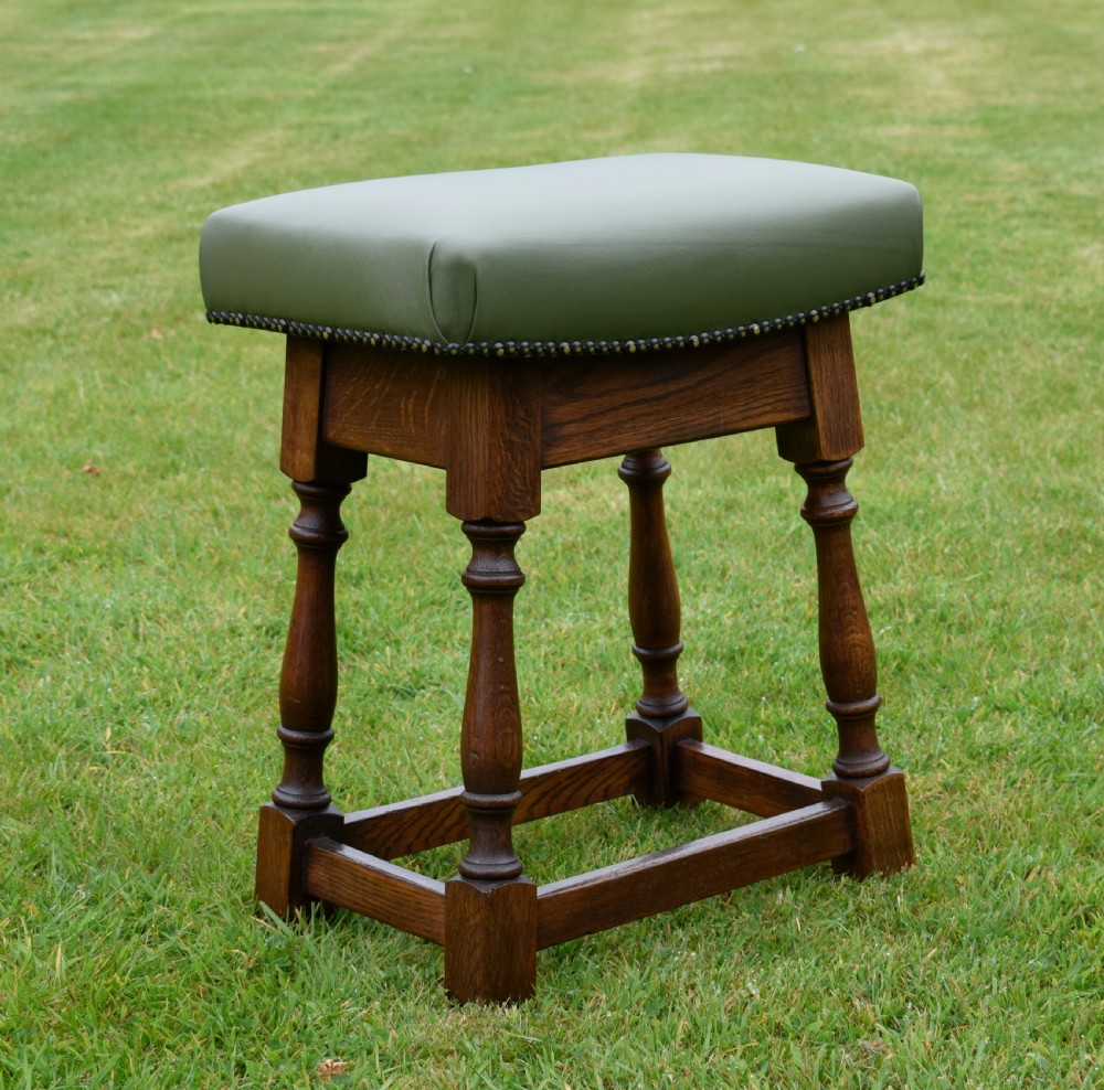 An early twentieth-century oak joint stool featuring an olive green leather upholstered seat secured with brass studs over turned legs. View VI