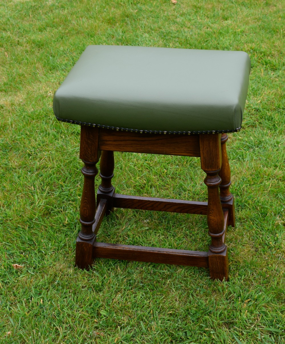 An early twentieth-century oak joint stool featuring an olive green leather upholstered seat secured with brass studs over turned legs. View VII