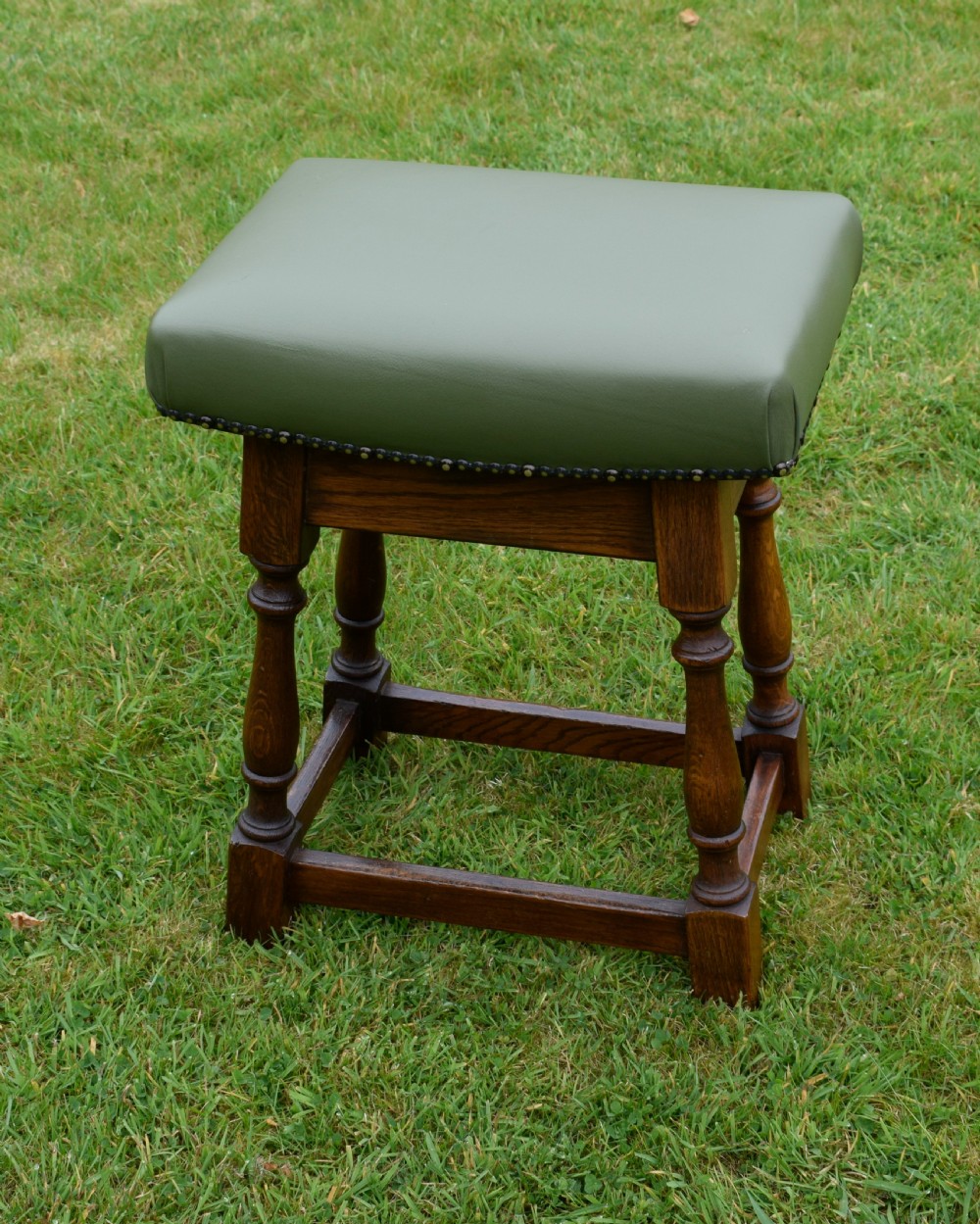 An early twentieth-century oak joint stool featuring an olive green leather upholstered seat secured with brass studs over turned legs. View VIII