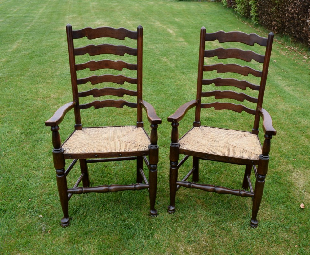 A pair of dark oak ladder back armchairs featuring woven rush seats, curved armrests, and turned front legs.
