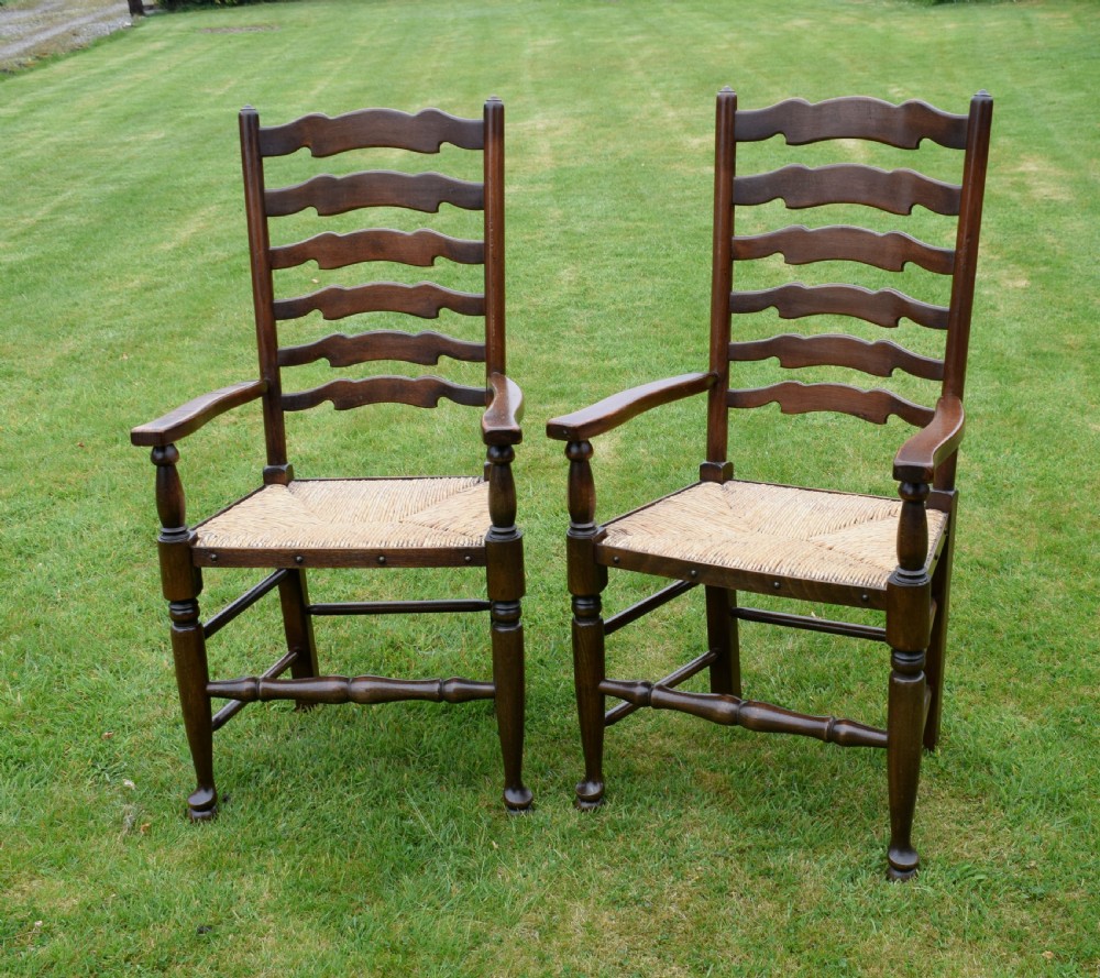 A pair of dark oak ladder back armchairs featuring woven rush seats, curved armrests, and turned front legs. View II