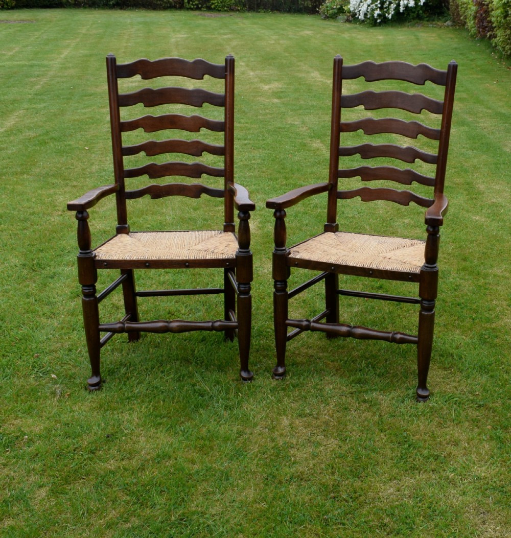A pair of dark oak ladder back armchairs featuring woven rush seats, curved armrests, and turned front legs. View III