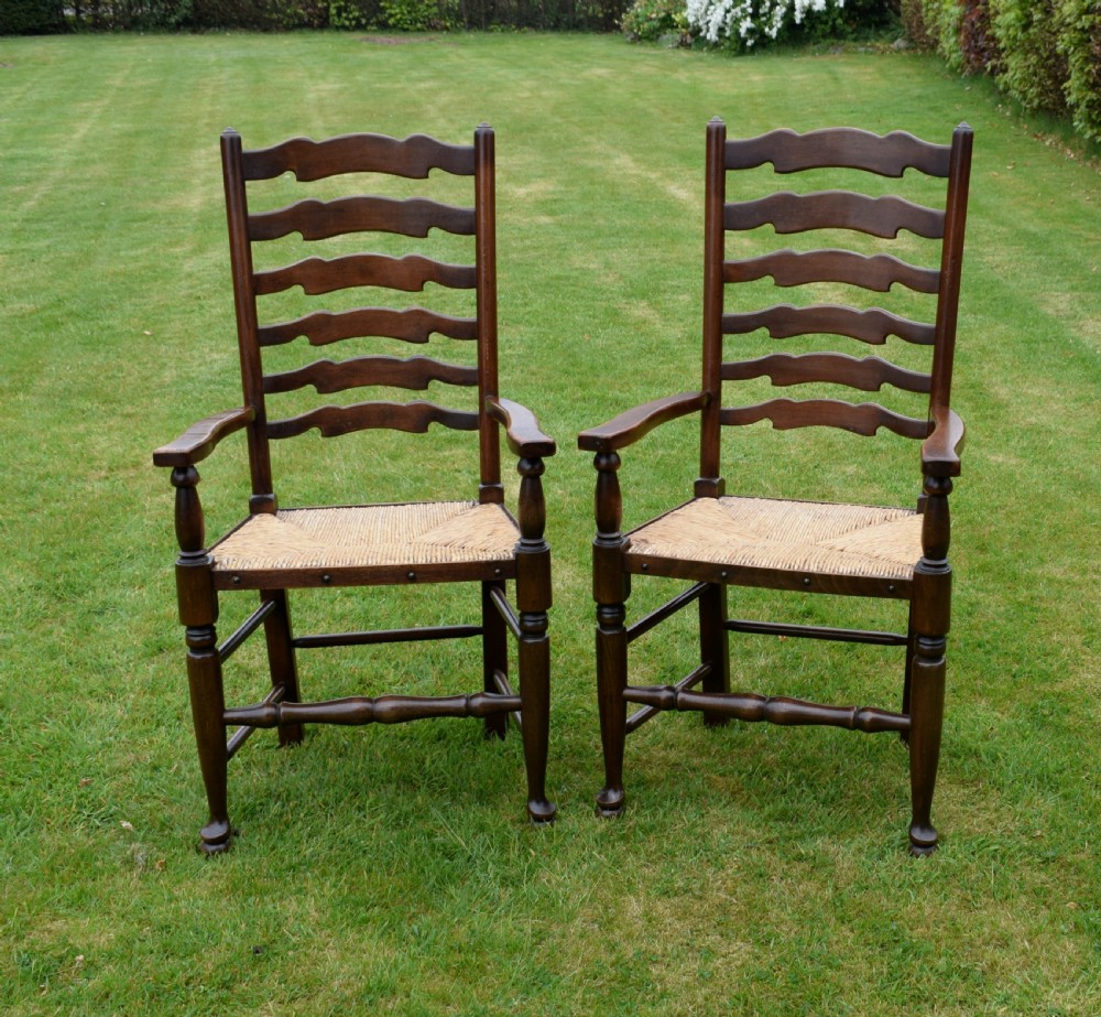 A pair of dark oak ladder back armchairs featuring woven rush seats, curved armrests, and turned front legs. View V