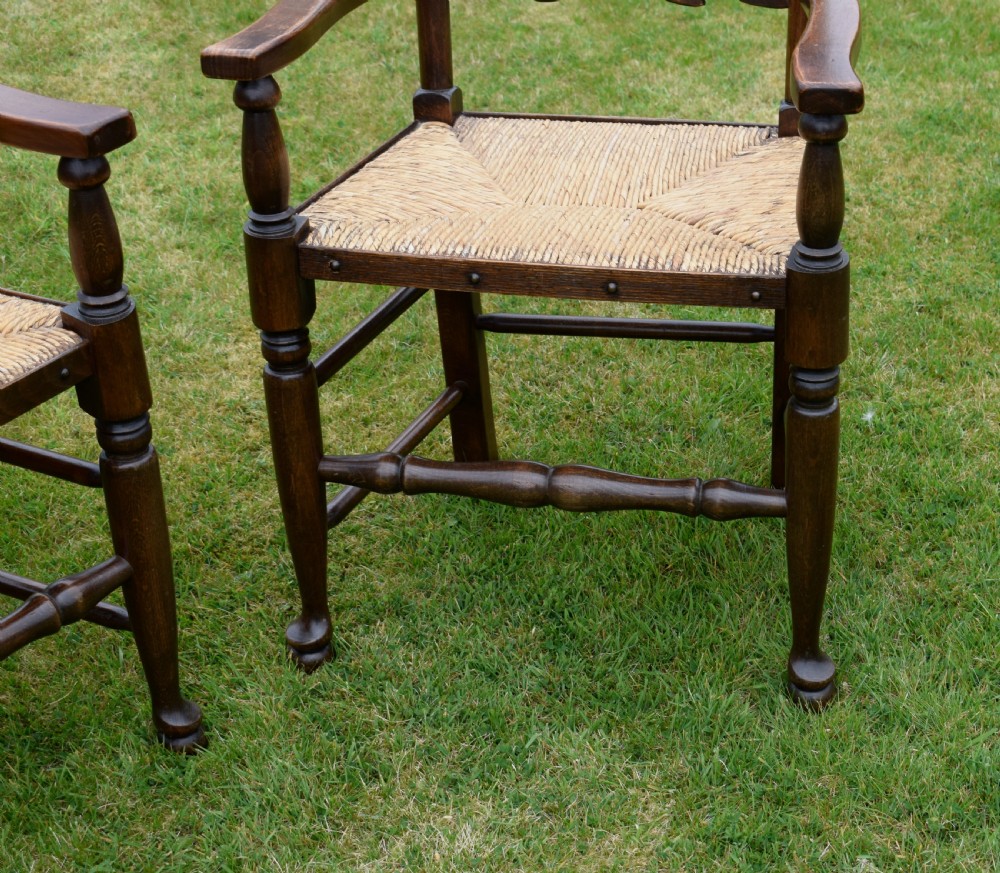 A pair of dark oak ladder back armchairs featuring woven rush seats, curved armrests, and turned front legs. View VI