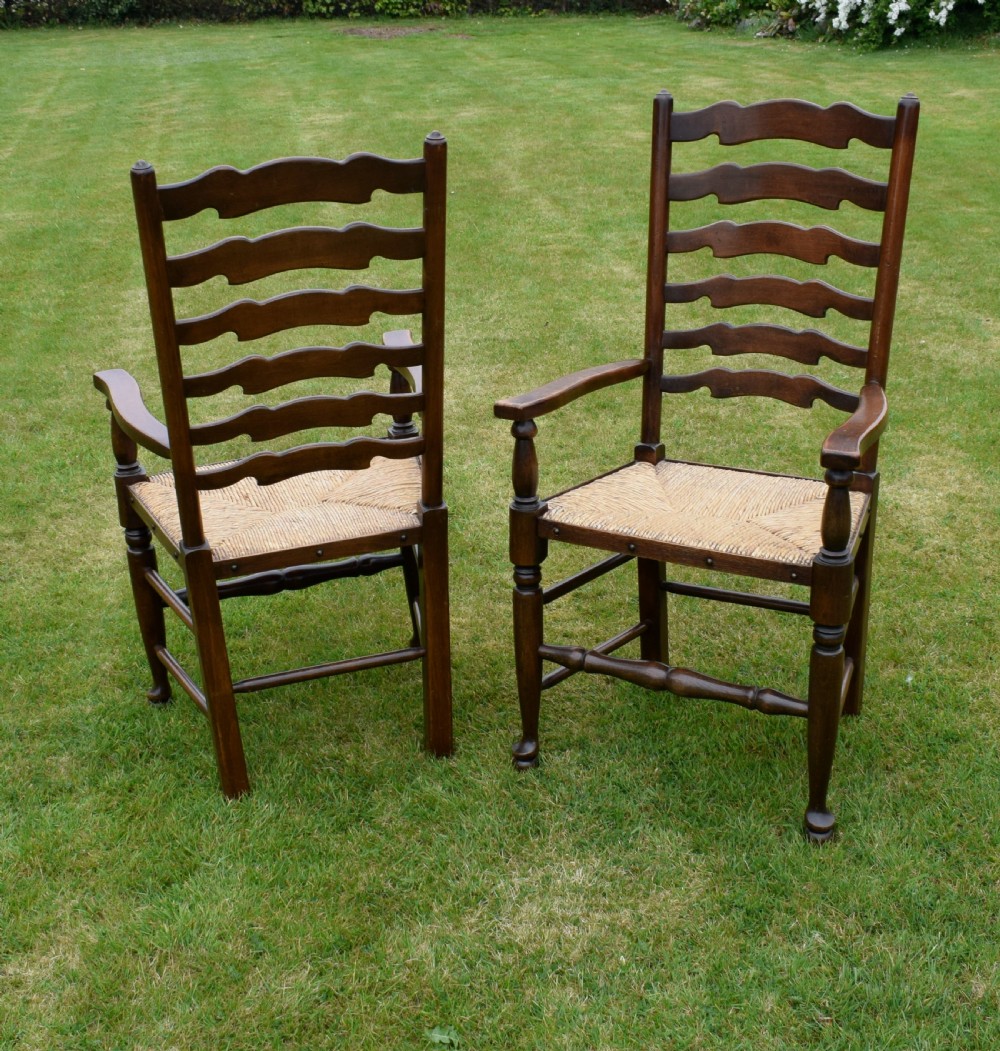 A pair of dark oak ladder back armchairs featuring woven rush seats, curved armrests, and turned front legs. View IX