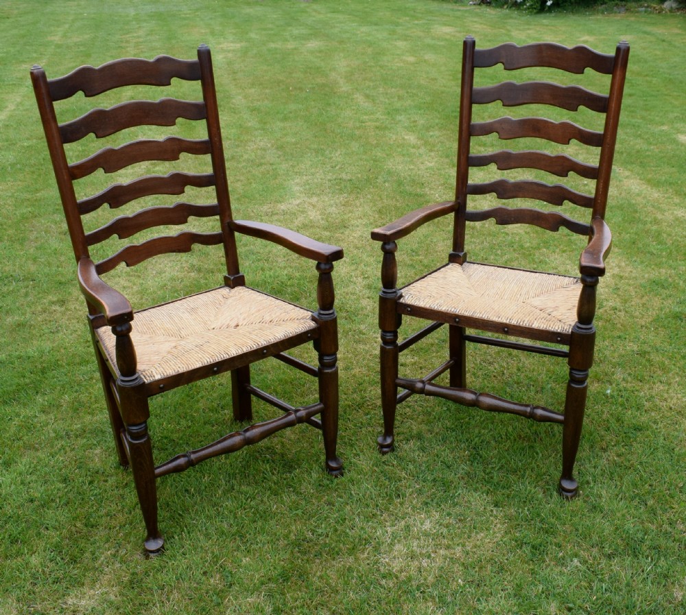 A pair of dark oak ladder back armchairs featuring woven rush seats, curved armrests, and turned front legs. View X