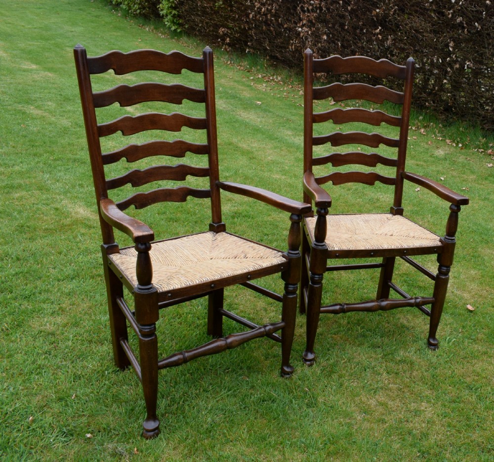 A pair of dark oak ladder back armchairs featuring woven rush seats, curved armrests, and turned front legs. View XII