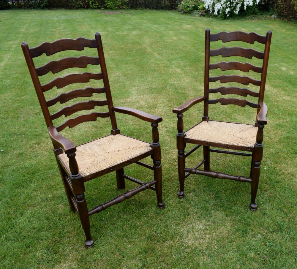A pair of dark oak ladder back armchairs featuring woven rush seats, curved armrests, and turned front legs. View XIII