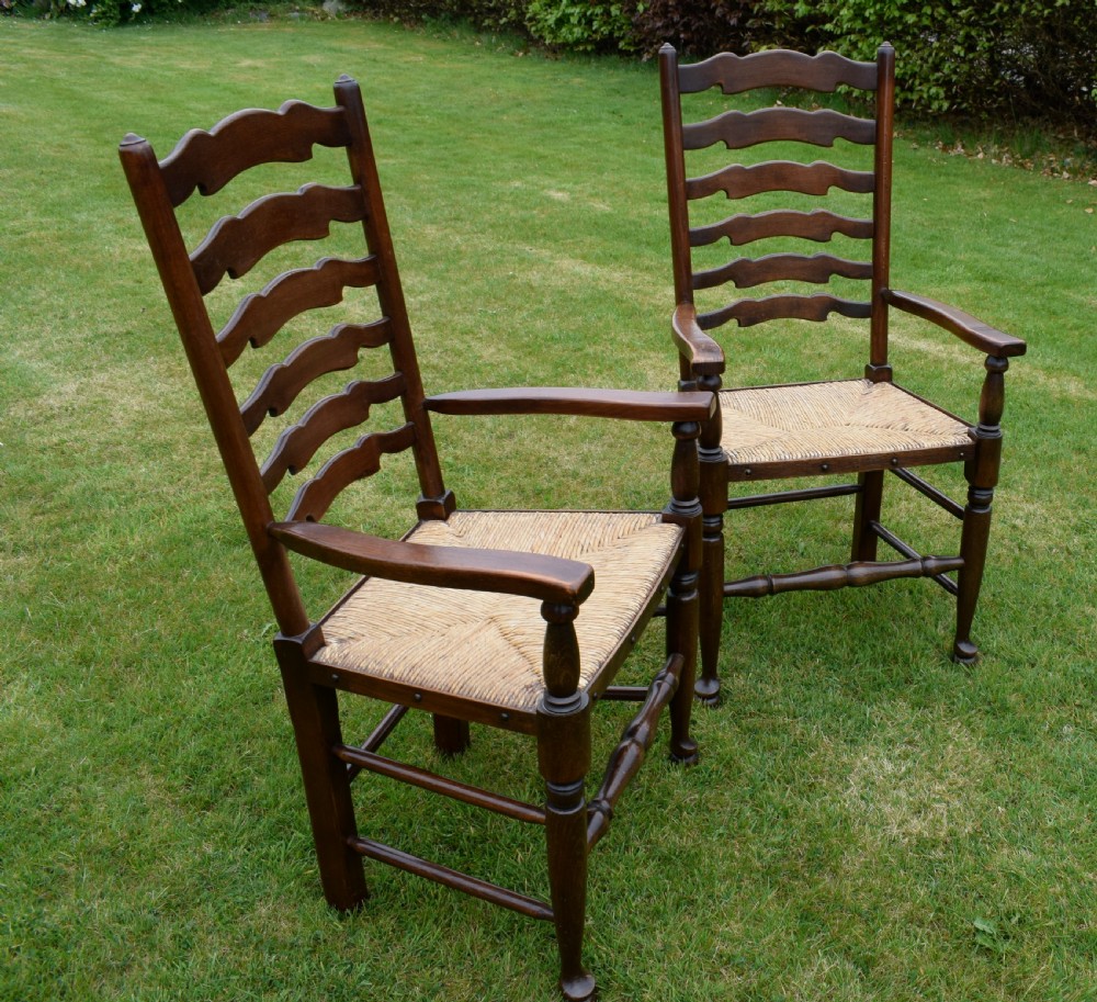 A pair of dark oak ladder back armchairs featuring woven rush seats, curved armrests, and turned front legs. View XV