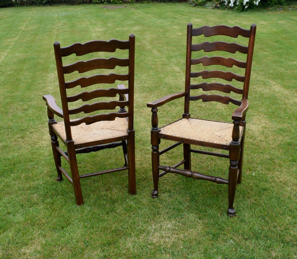 A pair of dark oak ladder back armchairs featuring woven rush seats, curved armrests, and turned front legs. View XVI