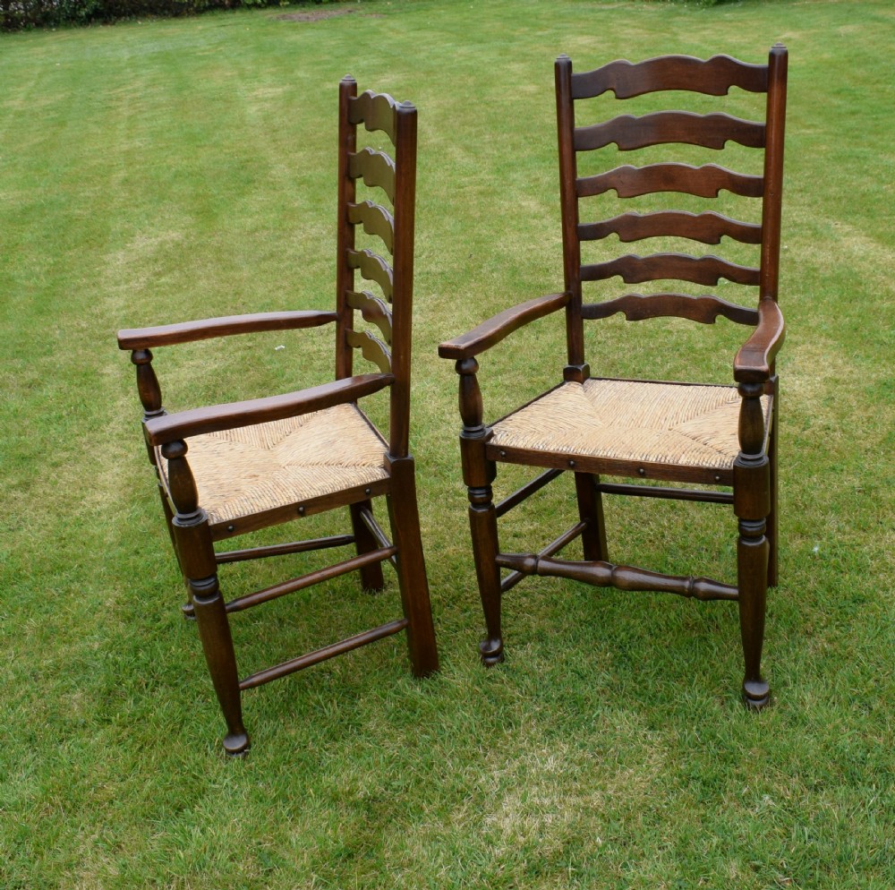 A pair of dark oak ladder back armchairs featuring woven rush seats, curved armrests, and turned front legs. View XVII