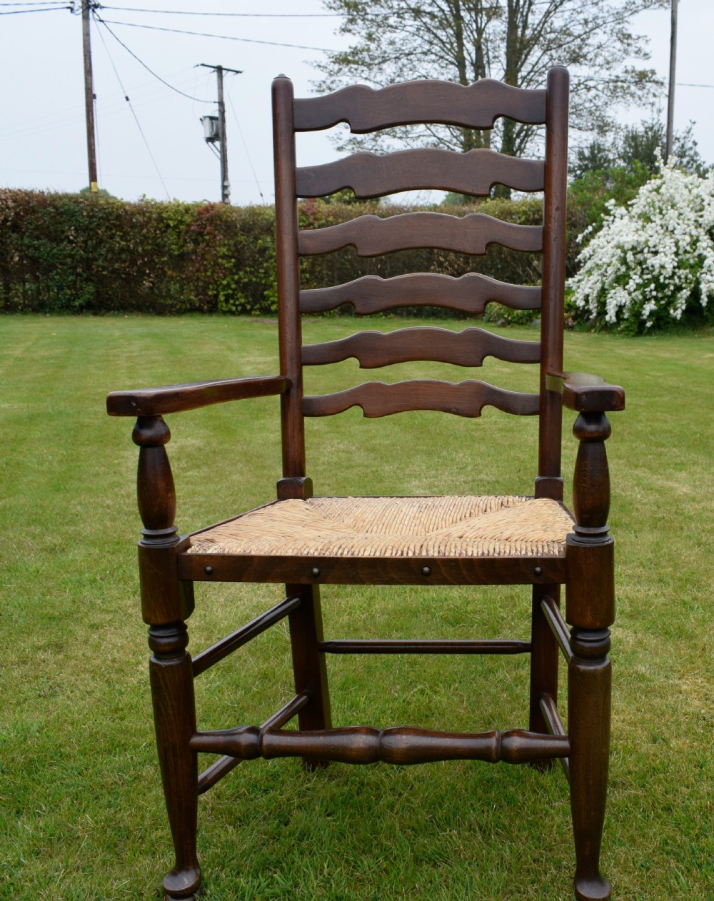 A pair of dark oak ladder back armchairs featuring woven rush seats, curved armrests, and turned front legs. View XIX